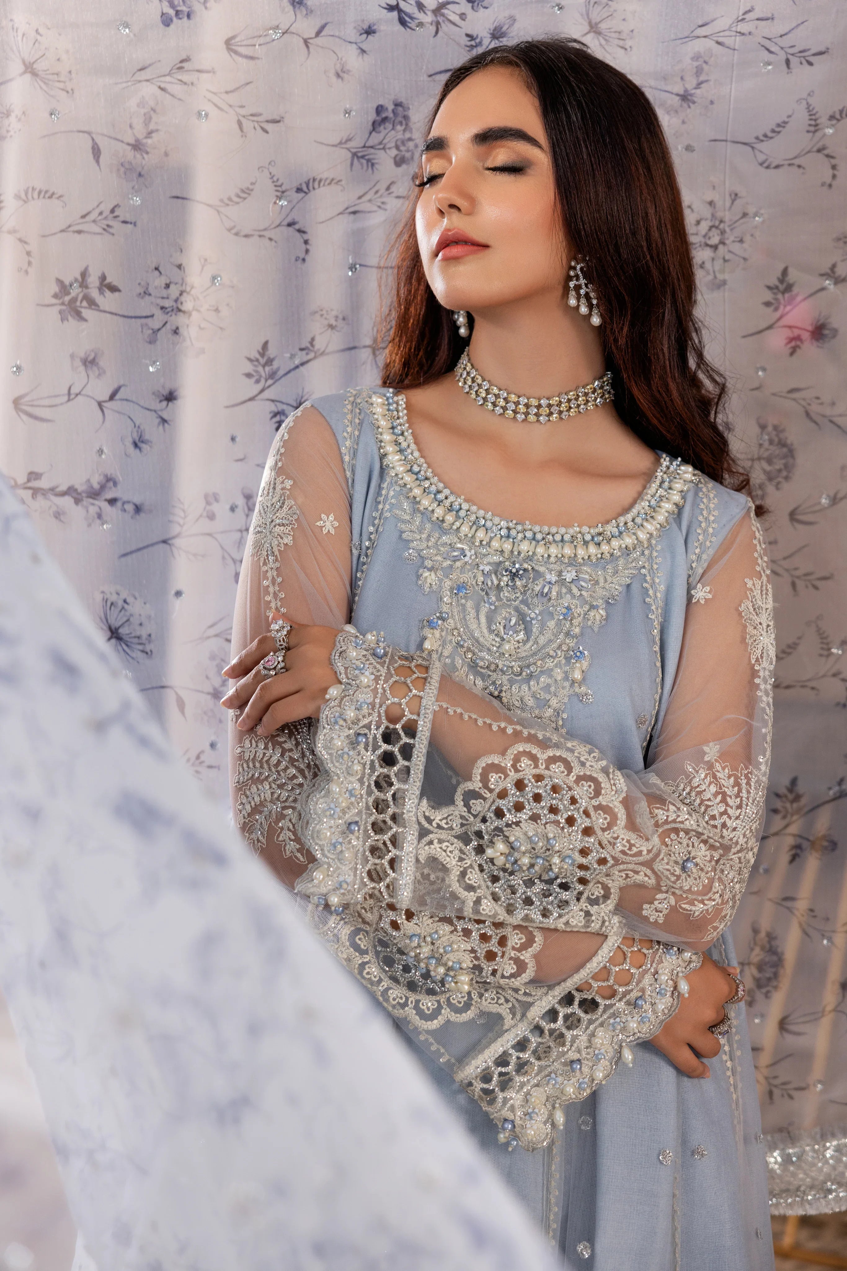 Woman in elegant blue embroidered formal dress from LA ELISE, posing with floral background
