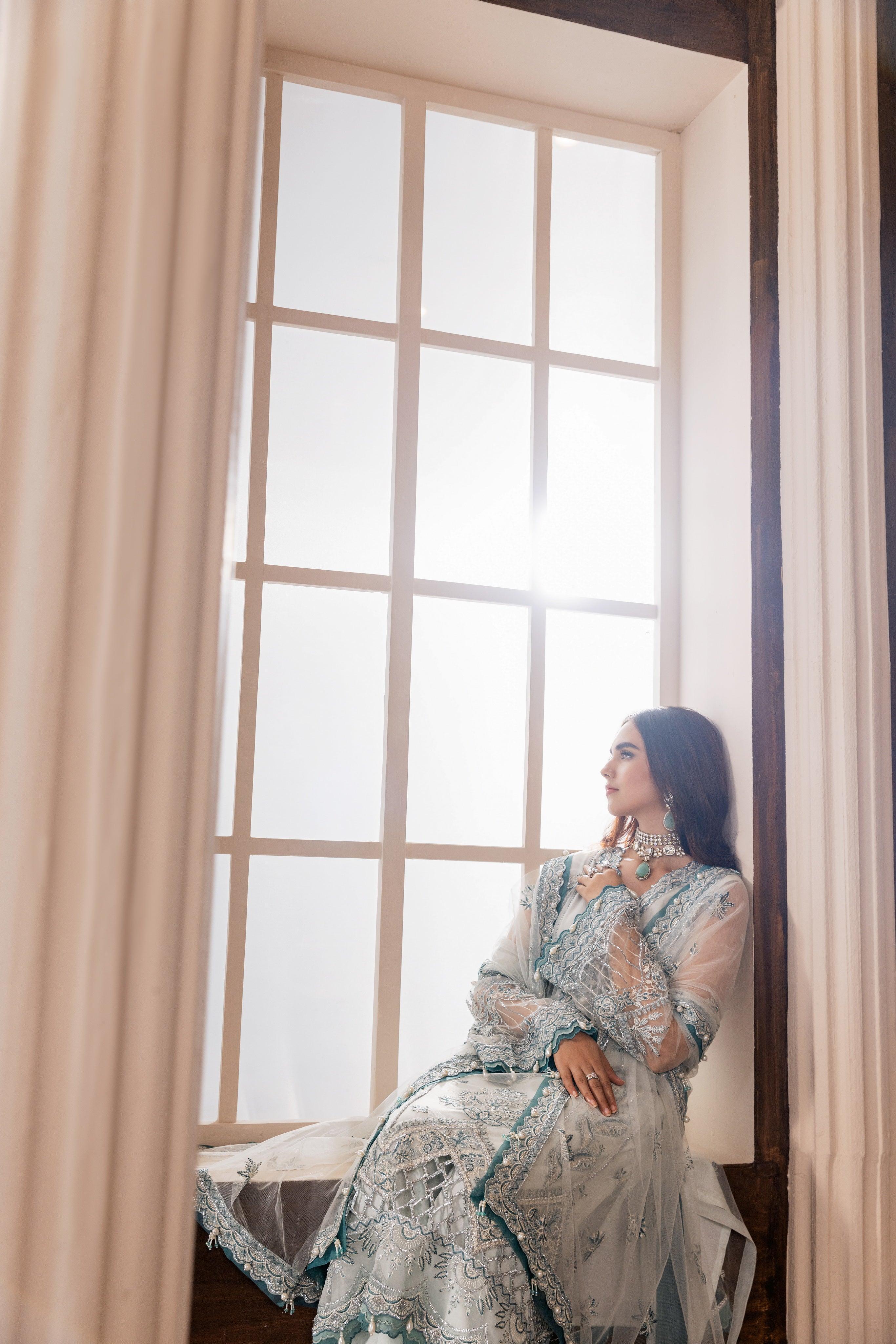 Woman in elegant unstitched embroidered dress sitting by window, LA ELISE women’s fashion