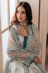 Woman in elegant embroidered teal and silver formal dress from LA ELISE near a window