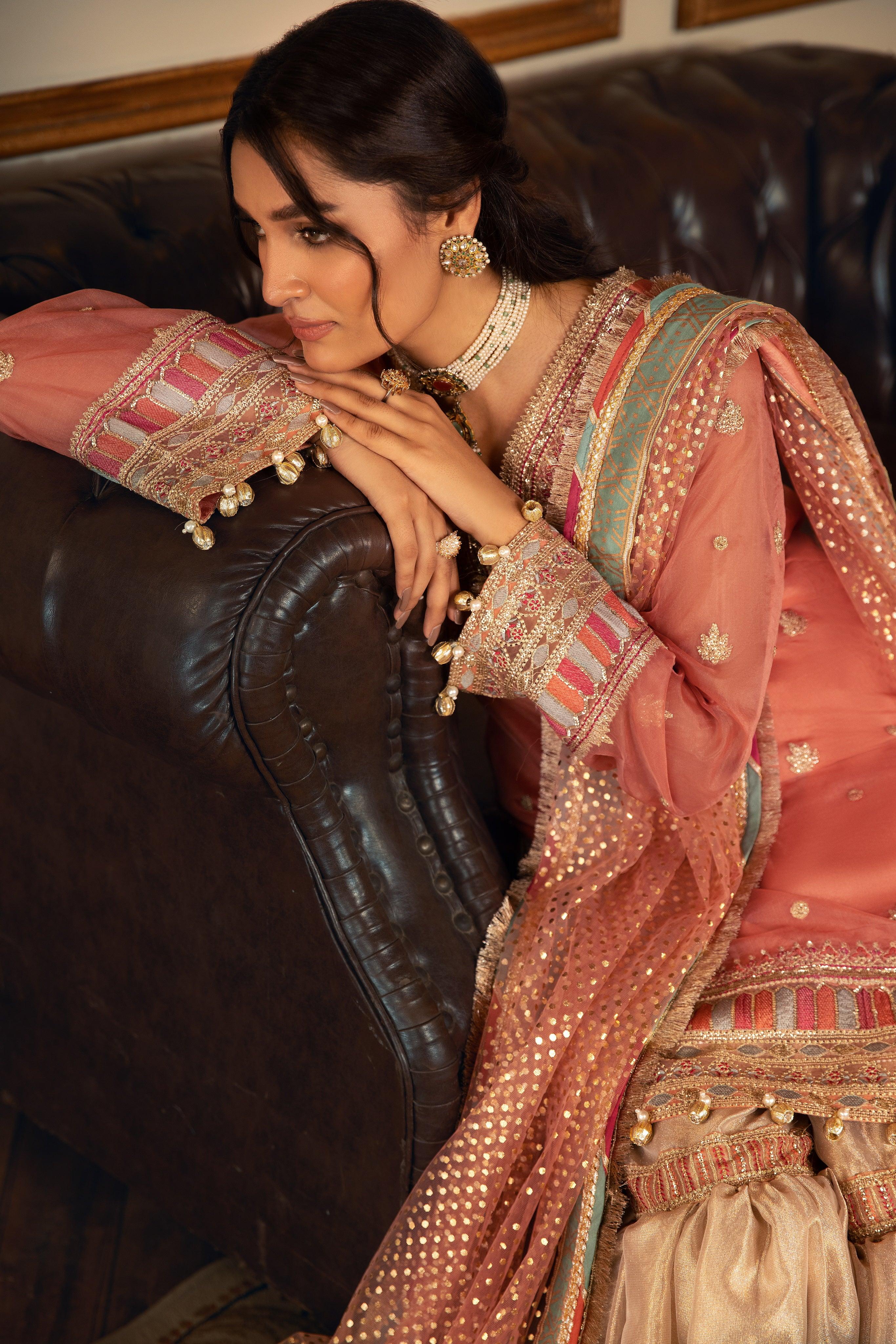 Woman in ornate peach and gold formal dress from LA ELISE, leaning on brown sofa