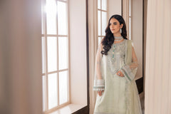 Woman in mint green embroidered formal dress by LA ELISE, standing by window