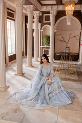 Woman in elegant blue embroidered formal dress from LA ELISE, seated in a classic interior with columns.