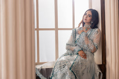 Woman in elegant blue embroidered formal dress by LA ELISE, sitting by a window indoors