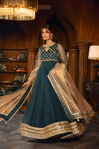 Woman in elegant blue and gold formal dress with sheer sleeves, posing in a classic library setting for LA ELISE women's fashion.